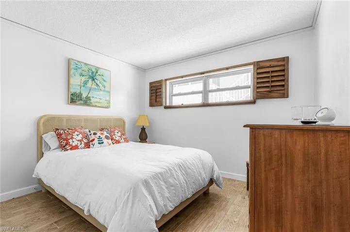 Wood-finish flooring with white baseboards, window with dark wood shutters, and white painted walls