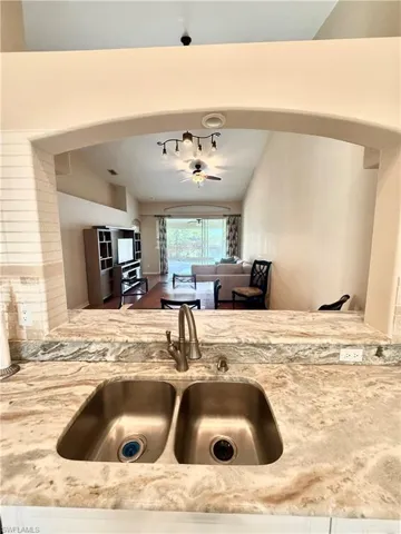 Kitchen with a ceiling fan, light stone counters, white cabinetry, and arched walkways