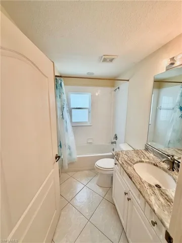 Full bathroom with vanity, a textured ceiling, shower / bath combination with curtain, and light tile patterned floors