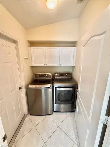 Laundry area featuring separate washer and dryer, light tile patterned flooring, and cabinet space