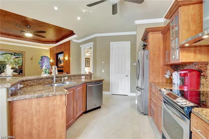 Kitchen with appliances with stainless steel finishes, wall chimney range hood, brown cabinets, a sink, and a ceiling fan