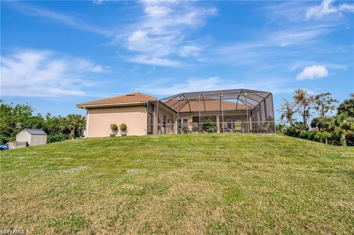 Back of property featuring a lawn, an outdoor structure, stucco siding, and glass enclosure