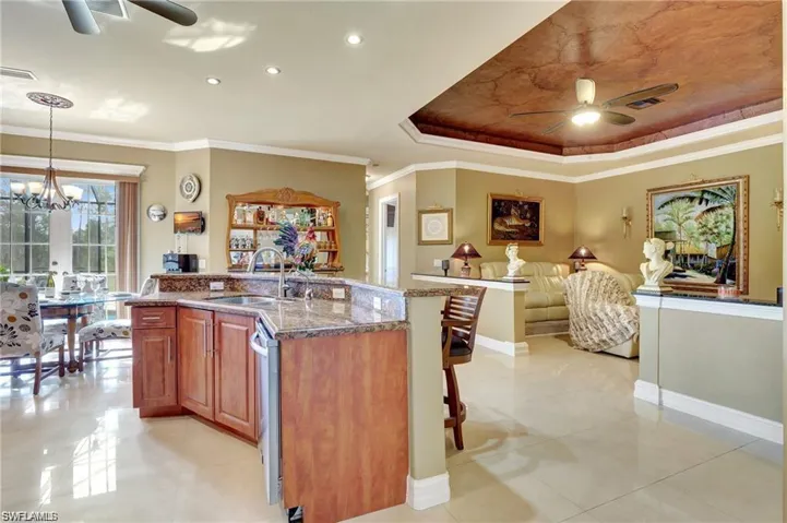 Kitchen with dark stone countertops, an island with sink, ceiling fan with notable chandelier, and a sink
