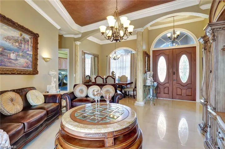 Foyer entrance with arched walkways, ornamental molding, ornate columns, a notable chandelier, and washer and clothes dryer
