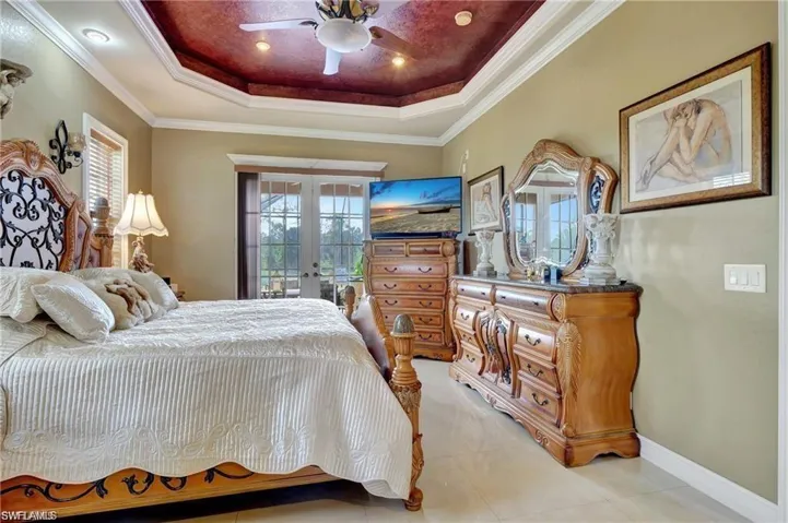 Bedroom with light tile patterned flooring, a raised ceiling, baseboards, ornamental molding, and french doors