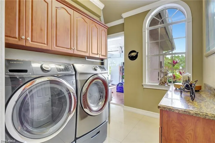 Laundry room featuring light tile patterned floors, crown molding, baseboards, separate washer and dryer, and cabinet space