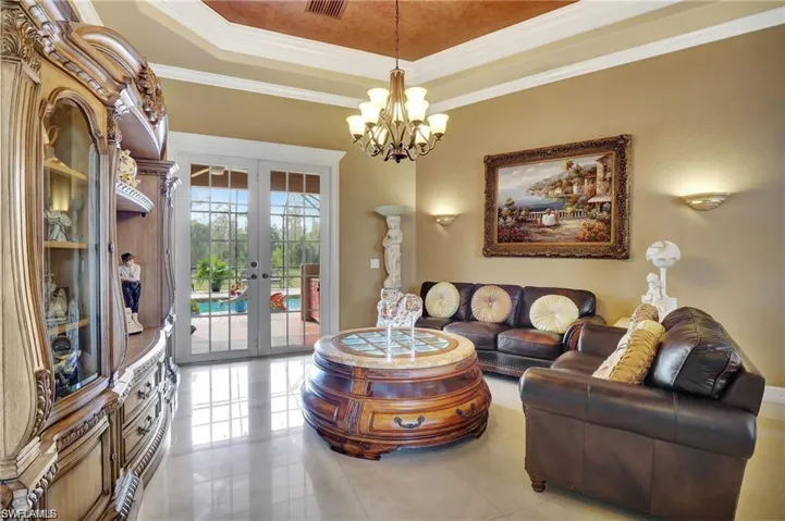 Living area with light tile patterned floors, a tray ceiling, ornamental molding, french doors, and a notable chandelier