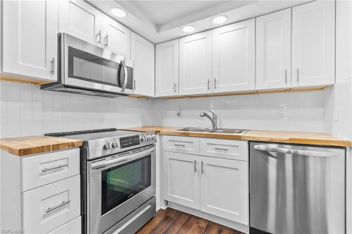 Kitchen with butcher block counters, appliances with stainless steel finishes, white cabinets, dark wood-type flooring, and recessed lighting