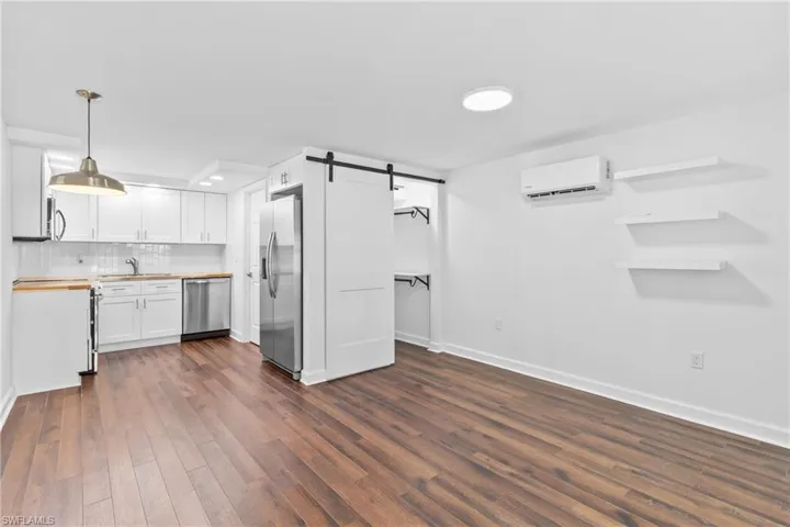 Kitchen with a barn door, tasteful backsplash, white cabinetry, appliances with stainless steel finishes, and hanging light fixtures