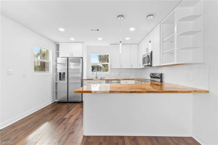 Kitchen with open shelves, white cabinetry, hanging light fixtures, wooden counters, and recessed lighting