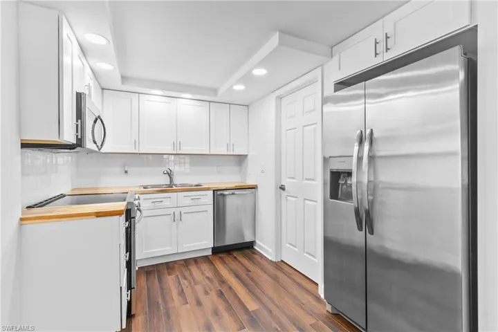 Kitchen featuring appliances with stainless steel finishes, recessed lighting, white cabinets, dark wood finished floors, and butcher block countertops