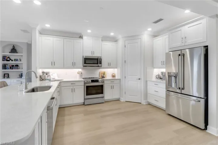 Kitchen with stainless steel appliances, visible vents, a sink, light wood-style floors, and white cabinetry