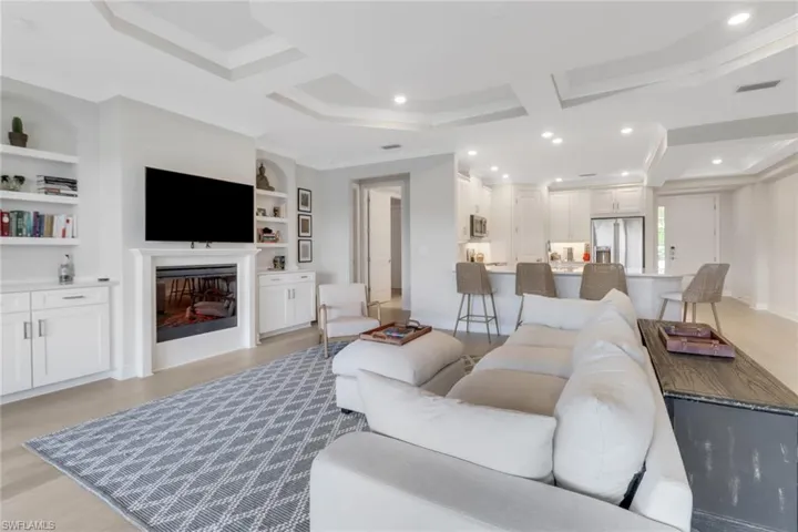 Living area featuring recessed lighting, coffered ceiling, visible vents, ornamental molding, and a glass covered fireplace