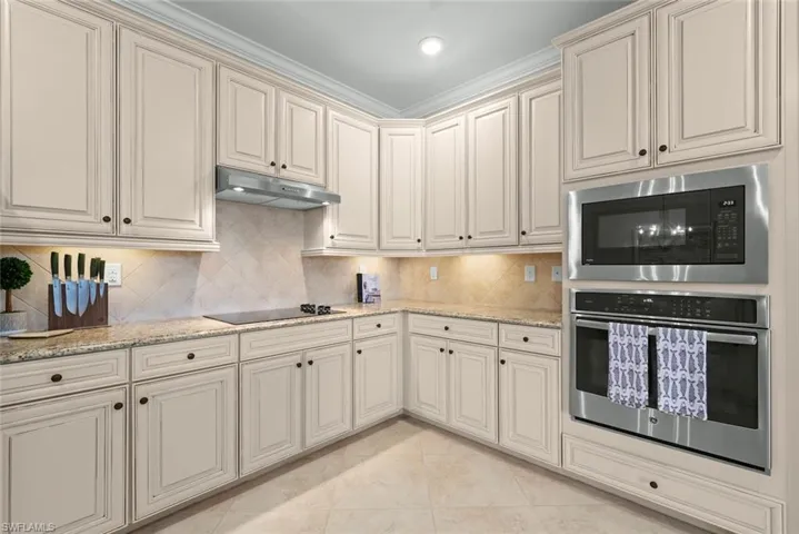 Kitchen featuring light-toned cabinetry with dark hardware, stone countertops, and a full tile backsplash