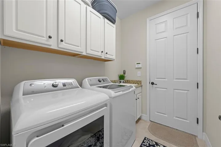 Dedicated laundry area featuring upper white cabinets for storage, washer, dryer and laundry tub.