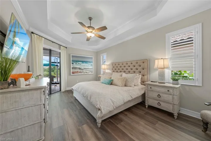 Primary bedroom with new luxury vinyl flooring, tray ceiling with crown molding, ceiling fan, and sliding glass door access to the outdoor area