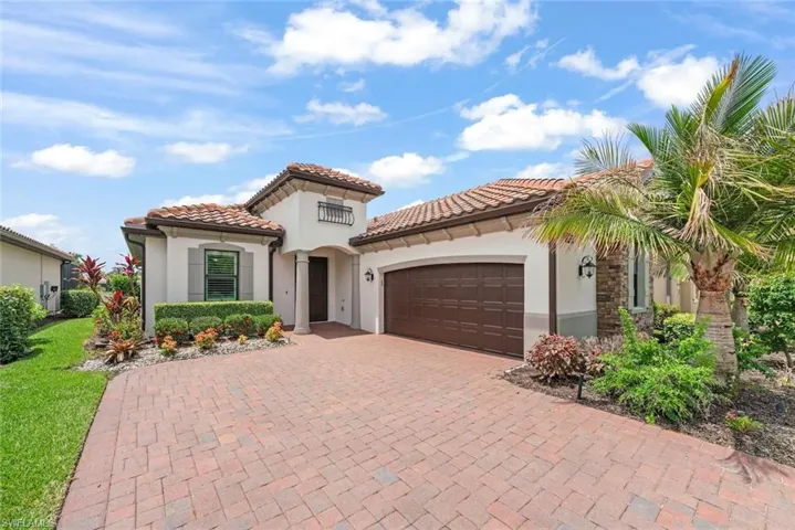 Newly painted front of a Twin Eagles single family home with a 2 car garage, tile roof, brick paver driveway and lush landscaping