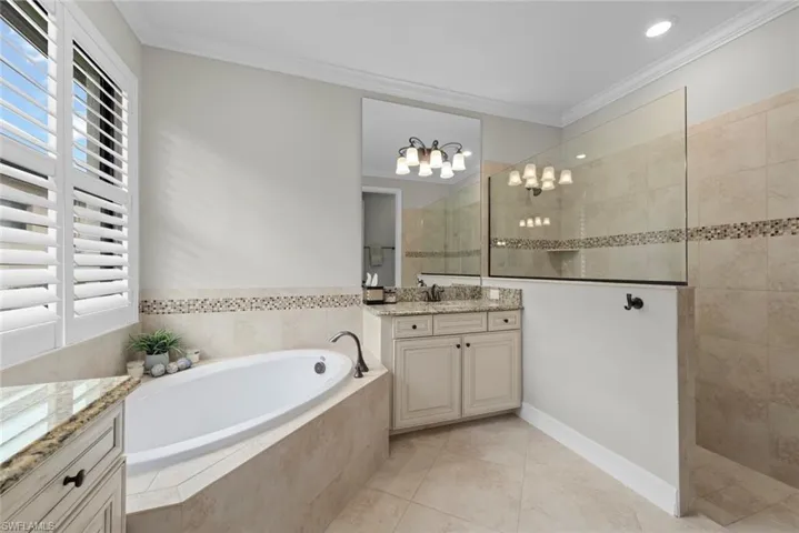 Spacious bathroom featuring a built-in soaking tub with a tiled surround, plantation shutters, and a glass-enclosed shower
