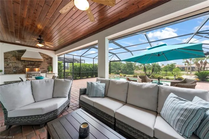 Screened outdoor living area featuring a wood-paneled ceiling, brick paver flooring, and an integrated outdoor kitchen with a built-in grill.