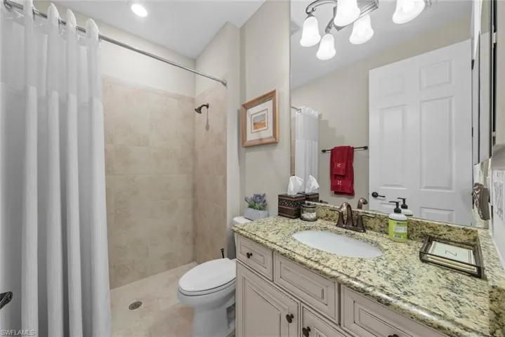 Guest bathroom featuring a walk-in shower, single vanity with a granite countertop, and a vanity-width mirror