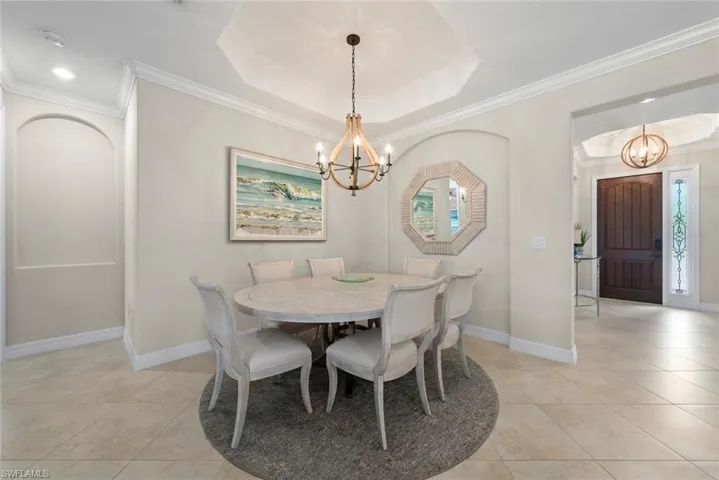 Dining area featuring a tray ceiling with a chandelier, tile flooring, crown molding, and an arched wall niche