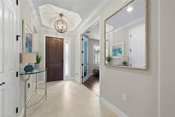 Foyer with tile flooring, a dark wood-finish entry door with decorative sidelight, a tray ceiling with a spherical chandelier, and crown molding