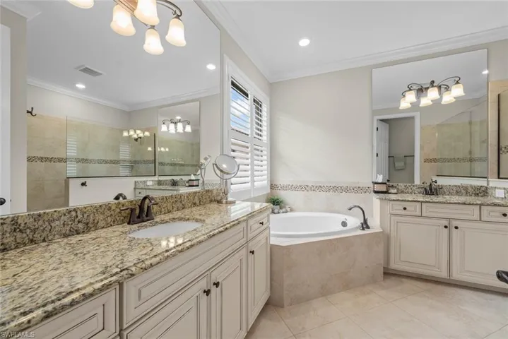 Primary bathroom with double vanity featuring light-toned cabinetry and granite countertops, bathtub and standalone shower.