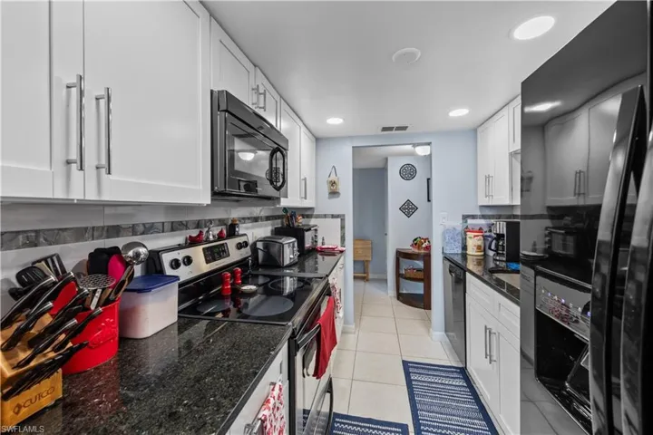 Kitchen with black appliances, white cabinets, dark stone counters, decorative backsplash, and light tile patterned floors