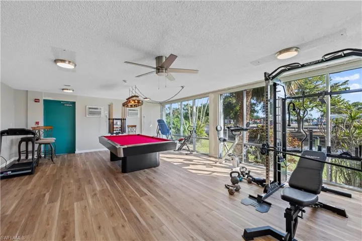 Game room featuring a wall of windows, billiards, a textured ceiling, a ceiling fan, and an AC wall unit