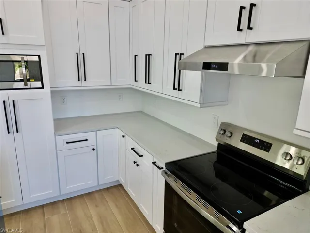 Kitchen with stainless steel appliances, light stone countertops, white cabinetry, and light wood-type flooring