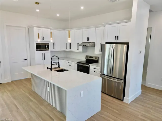 Kitchen featuring stainless steel appliances, light wood-style flooring, light stone counters, white cabinetry, and hanging light fixtures