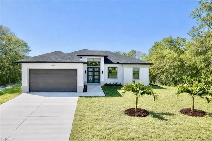 View of front facade featuring a front lawn, stucco siding, an attached garage, concrete driveway, and french doors