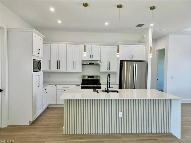 Kitchen with stainless steel appliances, light stone counters, decorative light fixtures, and white cabinetry