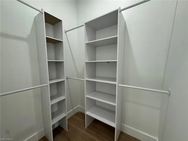 Walk in closet with dark wood-type flooring