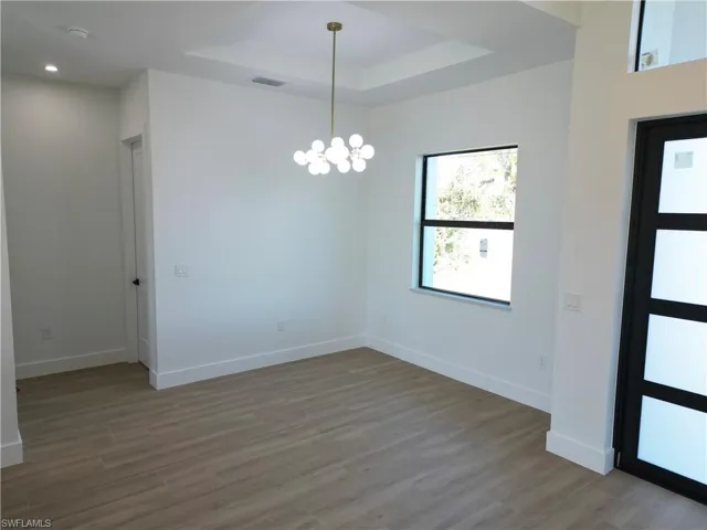 Entrance foyer with a tray ceiling, light wood-style flooring, and a chandelier