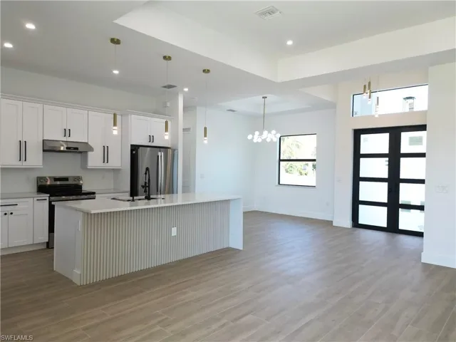 Kitchen featuring an island with sink, stainless steel appliances, white cabinets, and light wood-type flooring