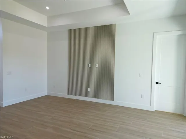Empty room featuring light wood-style floors, a raised ceiling, and recessed lighting