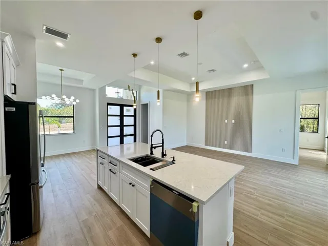 Kitchen with a tray ceiling, white cabinets, dishwasher, freestanding refrigerator, and open floor plan