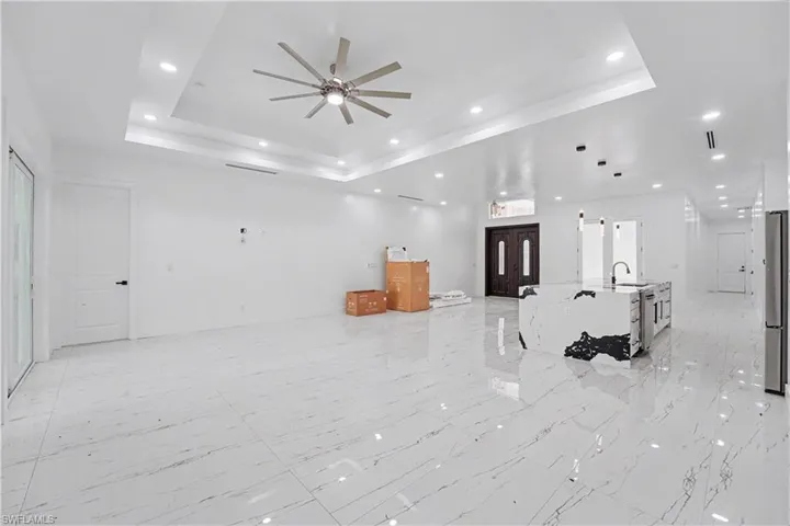 Open-concept living space featuring high ceilings with tray detailing and recessed lighting, large format polished tile flooring, and a contemporary ceiling fan