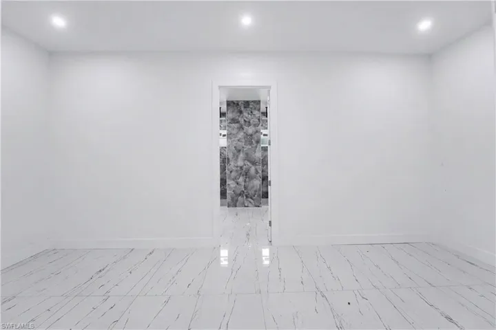 Spacious room featuring white walls, recessed ceiling lighting, and large format white tile flooring with dark veining