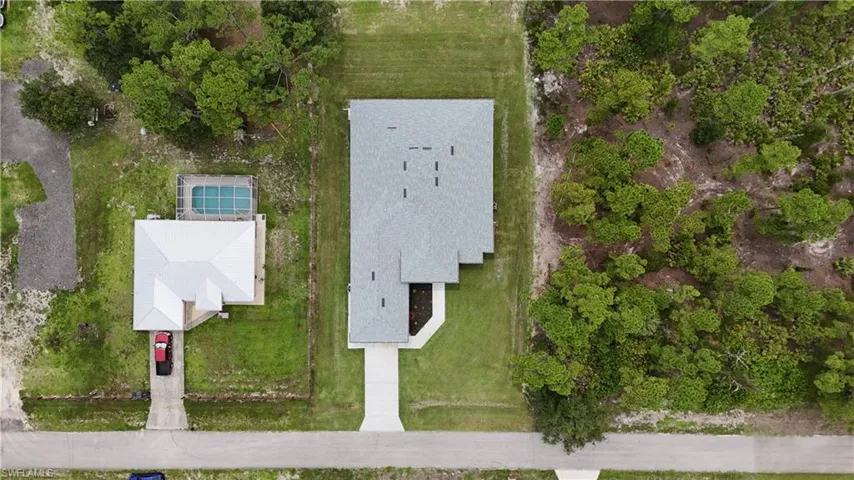 Property featuring a light gray roof, an expansive concrete driveway, and surrounding green lawn