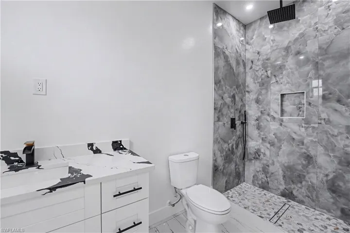Spacious shower featuring floor-to-ceiling marbled gray tile, a recessed niche, and a linear drain