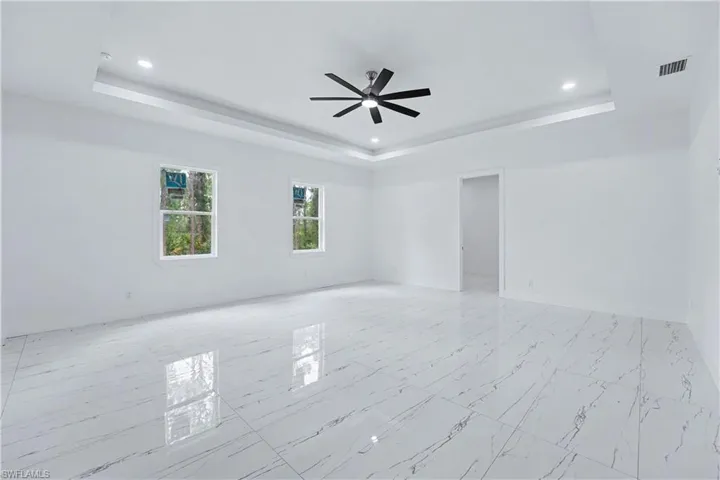 Spacious room featuring white walls, large format tile flooring, and a tray ceiling with recessed lighting