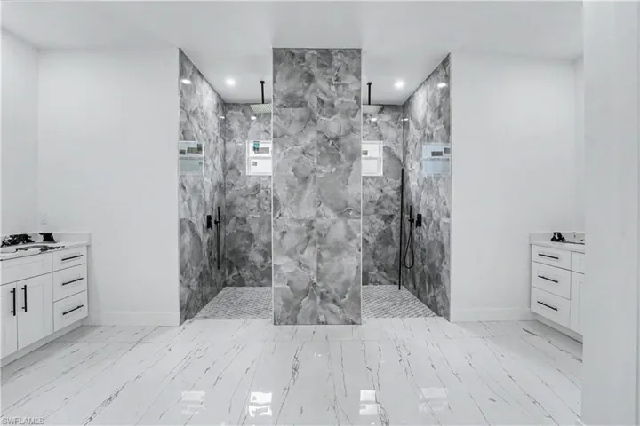 Spacious bathroom featuring two walk-in showers with grey-veined tile walls and mosaic tile flooring