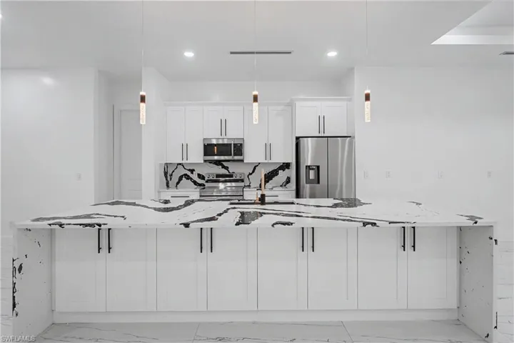 Modern kitchen featuring an expansive island with a waterfall countertop, white cabinetry, integrated stainless steel appliances, a striking black and white backsplash, and contemporary pendant lighting