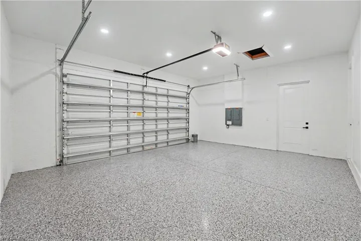 Spacious garage featuring epoxy flooring, overhead door with automatic opener, recessed lighting, and a paneled interior door