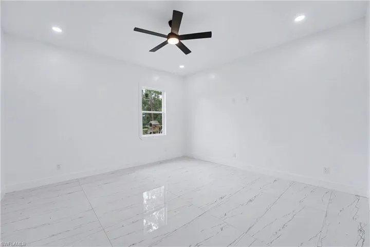 Spacious room featuring white walls, large format tile flooring, recessed lighting, a modern ceiling fan, and a single window