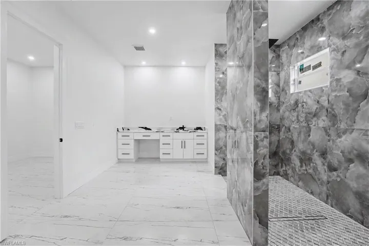 Spacious bathroom featuring large format marble-look floor tiles, a white double vanity with multiple drawers, and a walk-in shower with natural stone-look wall tiles and a mosaic tile floor