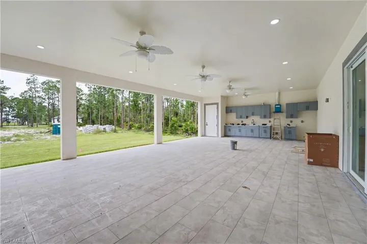 Expansive covered patio featuring large format tile flooring, an outdoor kitchen with cabinetry and sink, multiple ceiling fans, recessed lighting, and a sliding glass door entry