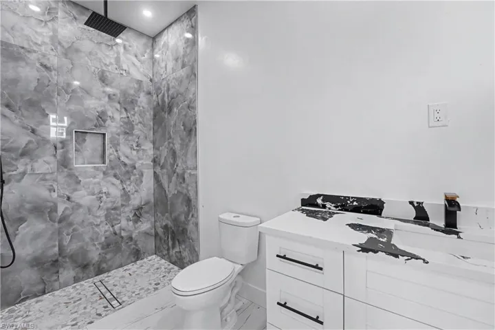 Modern bathroom featuring a tiled walk-in shower with a black rain showerhead, a built-in shower niche, and a pebble-tiled floor